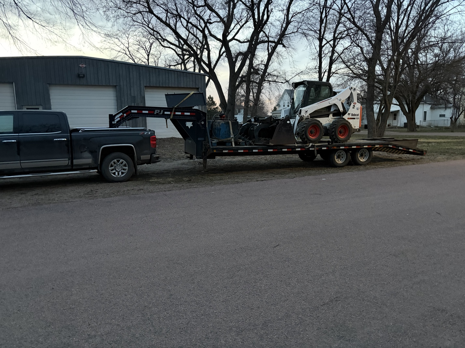 Truck, trailer, and Bobcat parked outside the SS Stump Grinding shop at dusk